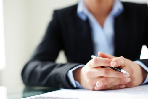 A female lawyer with her hands clasped together, holding a pen.